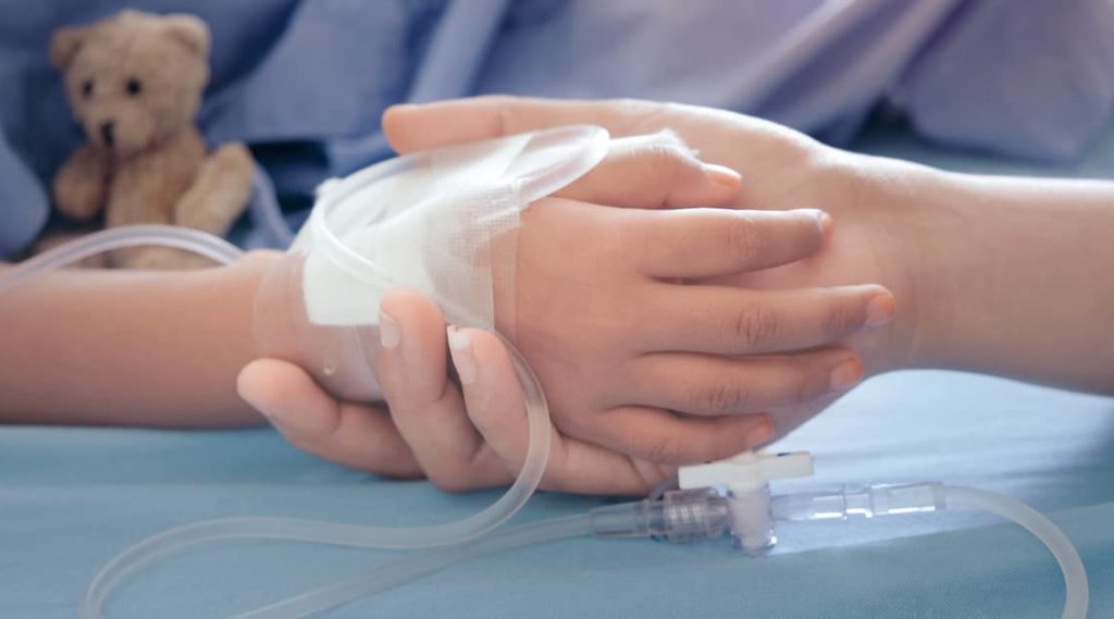 mother's hand grasping the hand of a sick child in a hospital bed