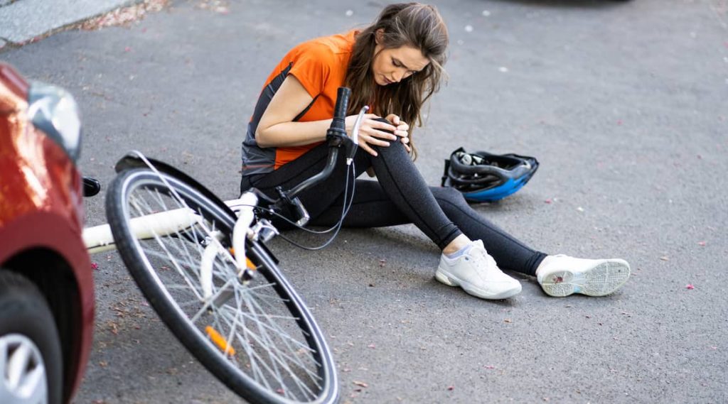 woman with injured knee lying on the ground after a bike accident