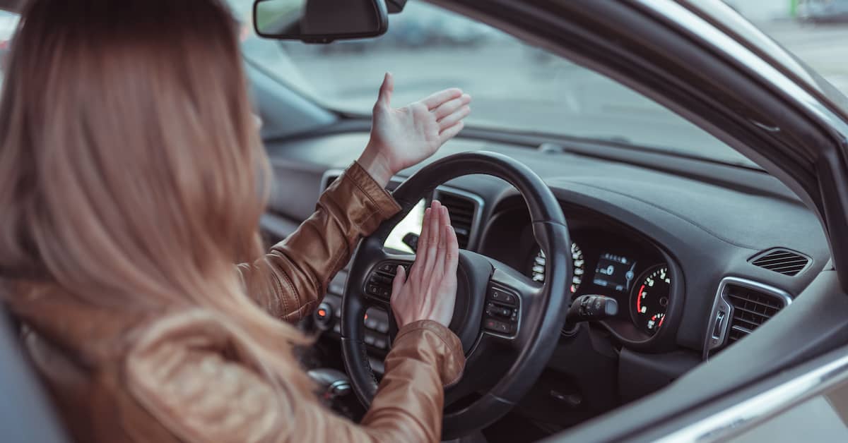 Young woman behind the wheel of a car honking at another motorist | Henry Carus + Associates