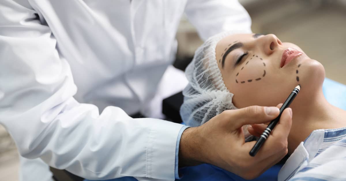 Cosmetic surgeon drawing lines on young woman's face for cosmetic surgery plan | Henry Carus + Associates