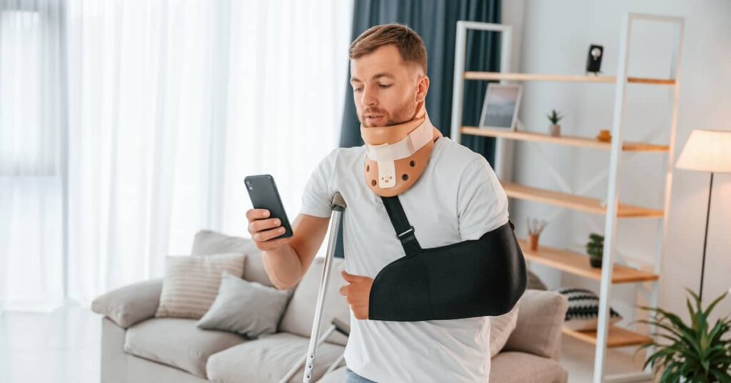 Young man with an injured arm and neck checking his mobile phone | Henry Carus + Associates